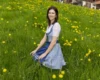 Woman in a blue dirndl sitting in a field of yellow dandelions, smiling at the camera.
